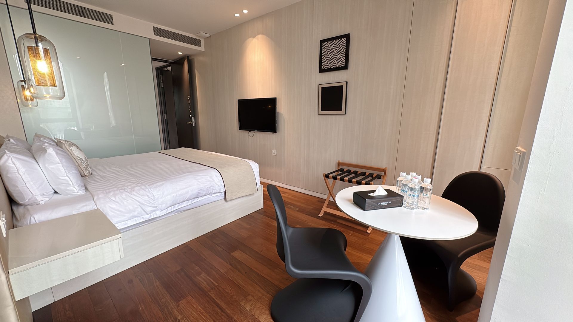 Modern hotel room with bed, small table, chairs, luggage rack, and TV.