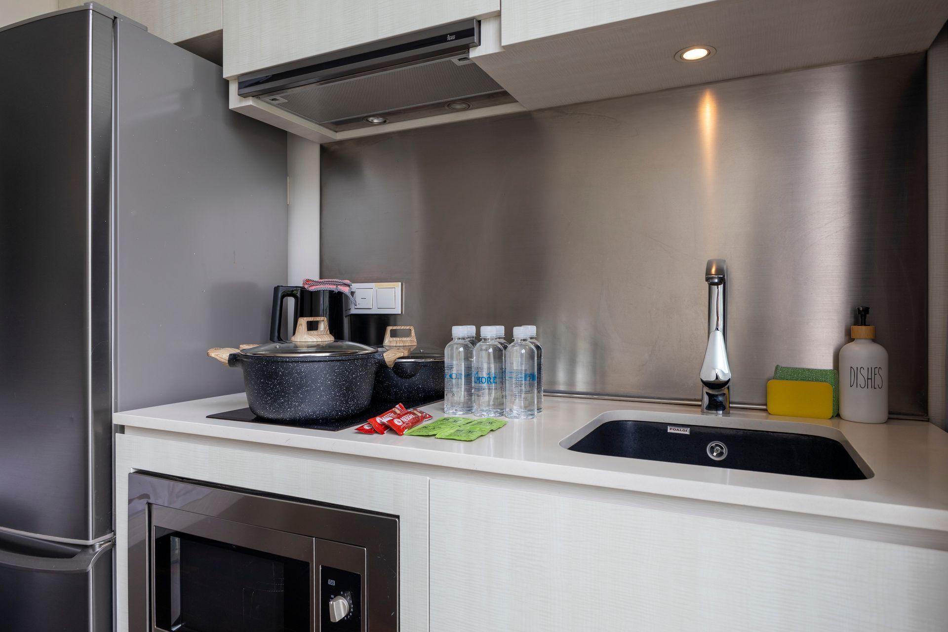 Small kitchen with stainless steel backsplash, sink, microwave, and refrigerator.