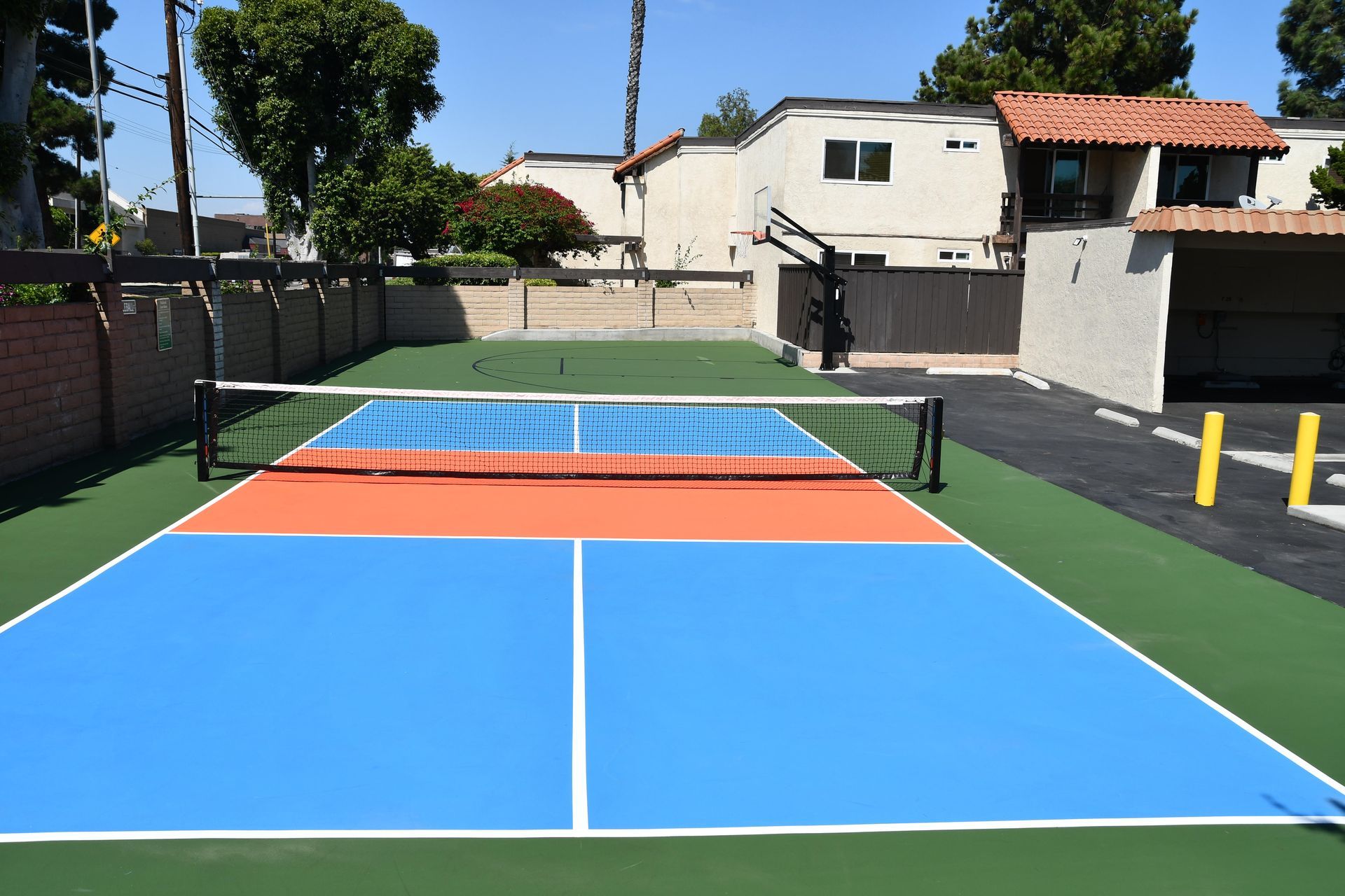 Pickleball court with blue and orange playing areas, net, and surrounding buildings.