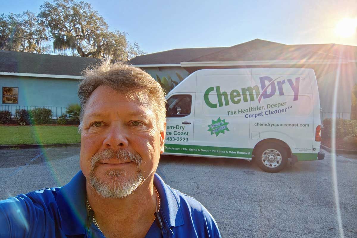 Man taking selfie in front of a Chem-Dry van in bright sunlight outside a building