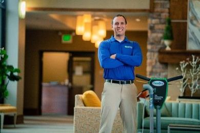 A Chem-Dry technician standing with a smile next to a floor cleaning machine in a lobby.