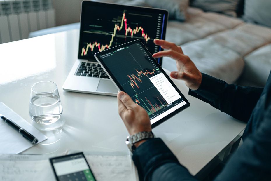 A person is holding a tablet with a graph on it in front of a laptop.