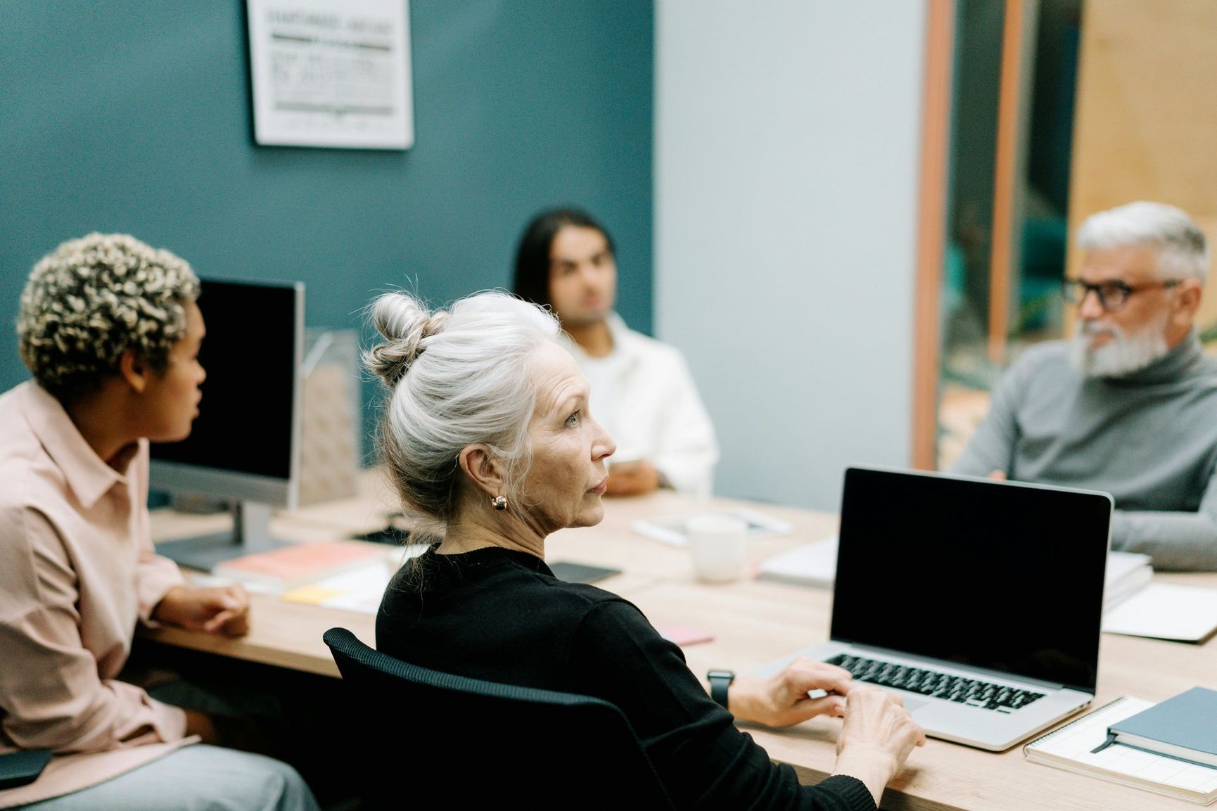 A group of people are sitting around a table with laptops.