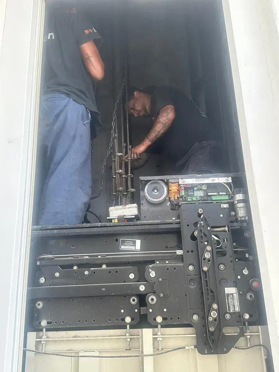 Dos trabajadores dentro de un compartimento de máquina negro inspeccionando componentes y cableado.