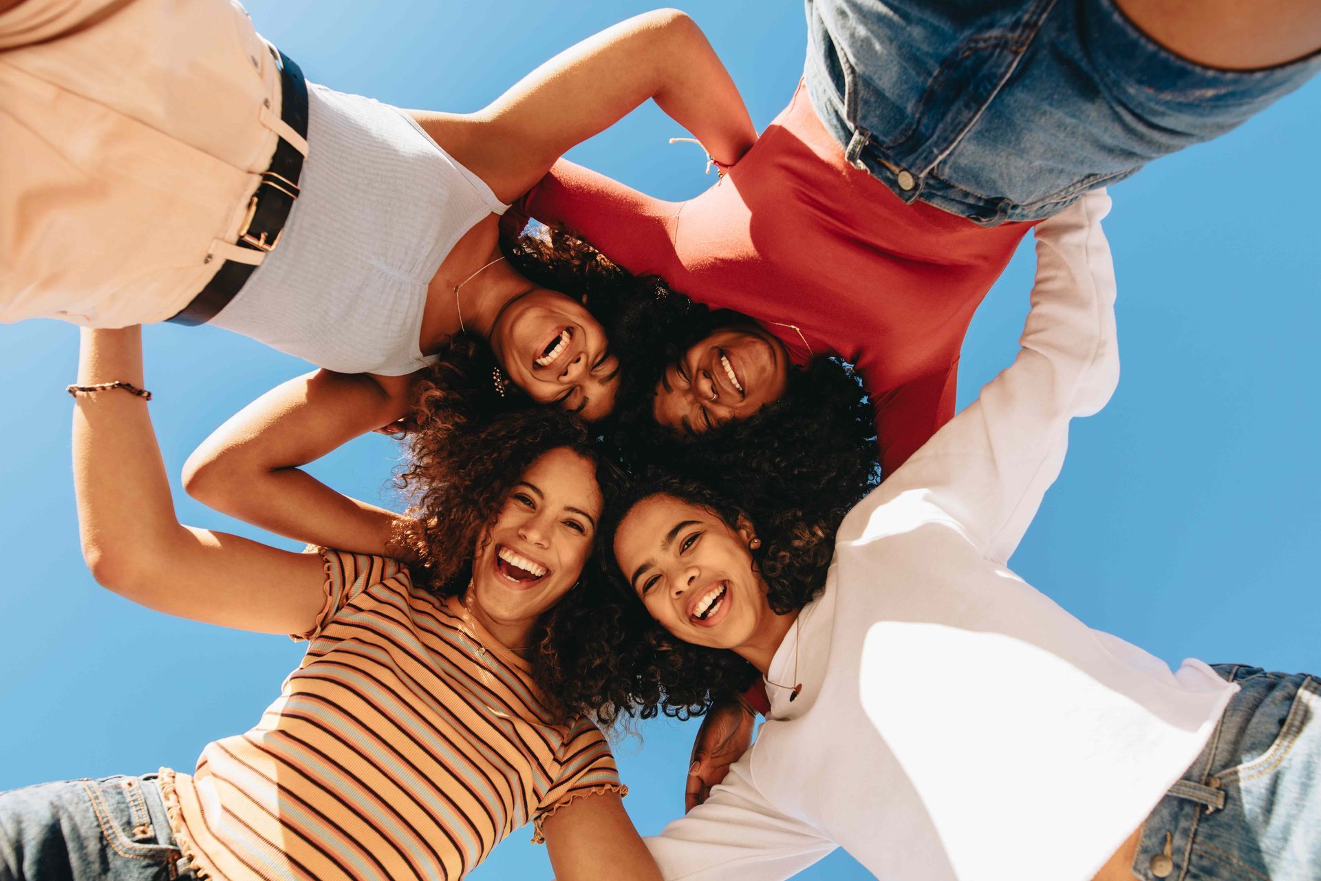 Four people smiling and embracing, seen from below, against a blue sky. Four people smiling and embracing, seen from below, against a blue sky.