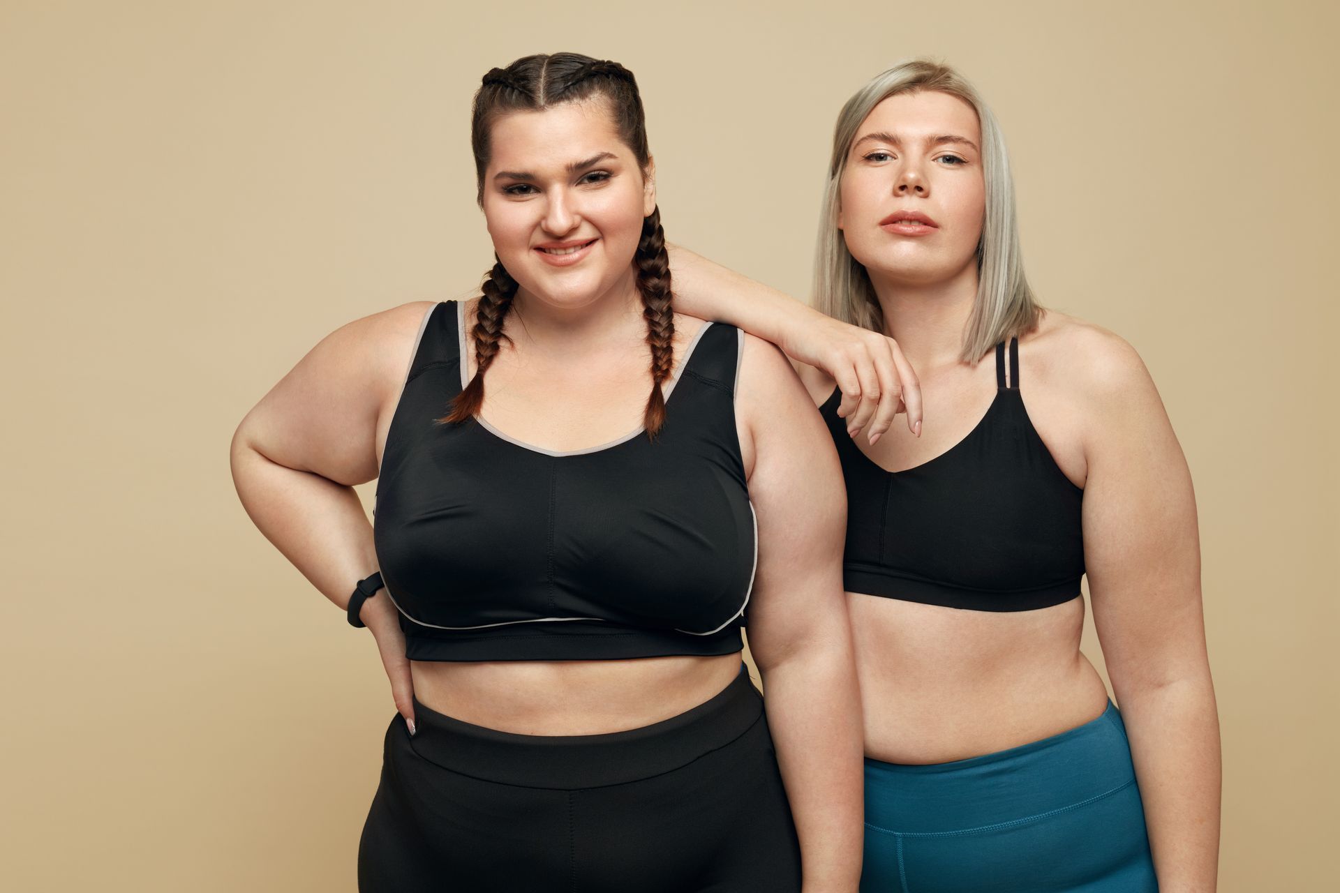 Two women in athletic wear pose together. One has braided hair, smiles, and the other has blonde hair, leans on her friend, and stares forward. Two women in athletic wear pose together. One has braided hair, smiles, and the other has blonde hair, leans on her friend, and stares forward.