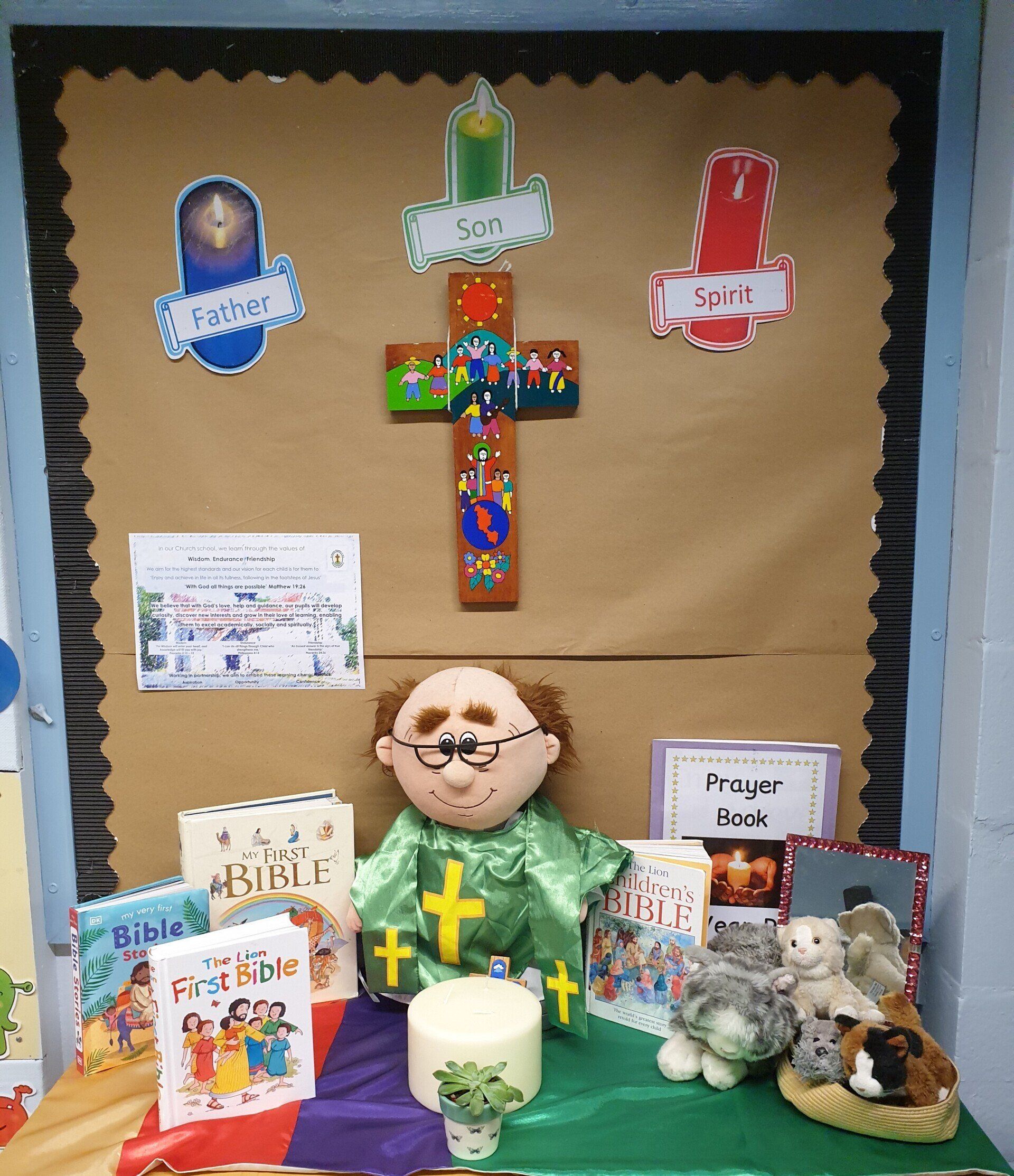 A religious display featuring a cross, books, a doll, and candles. Brown backdrop, colorful decorations.