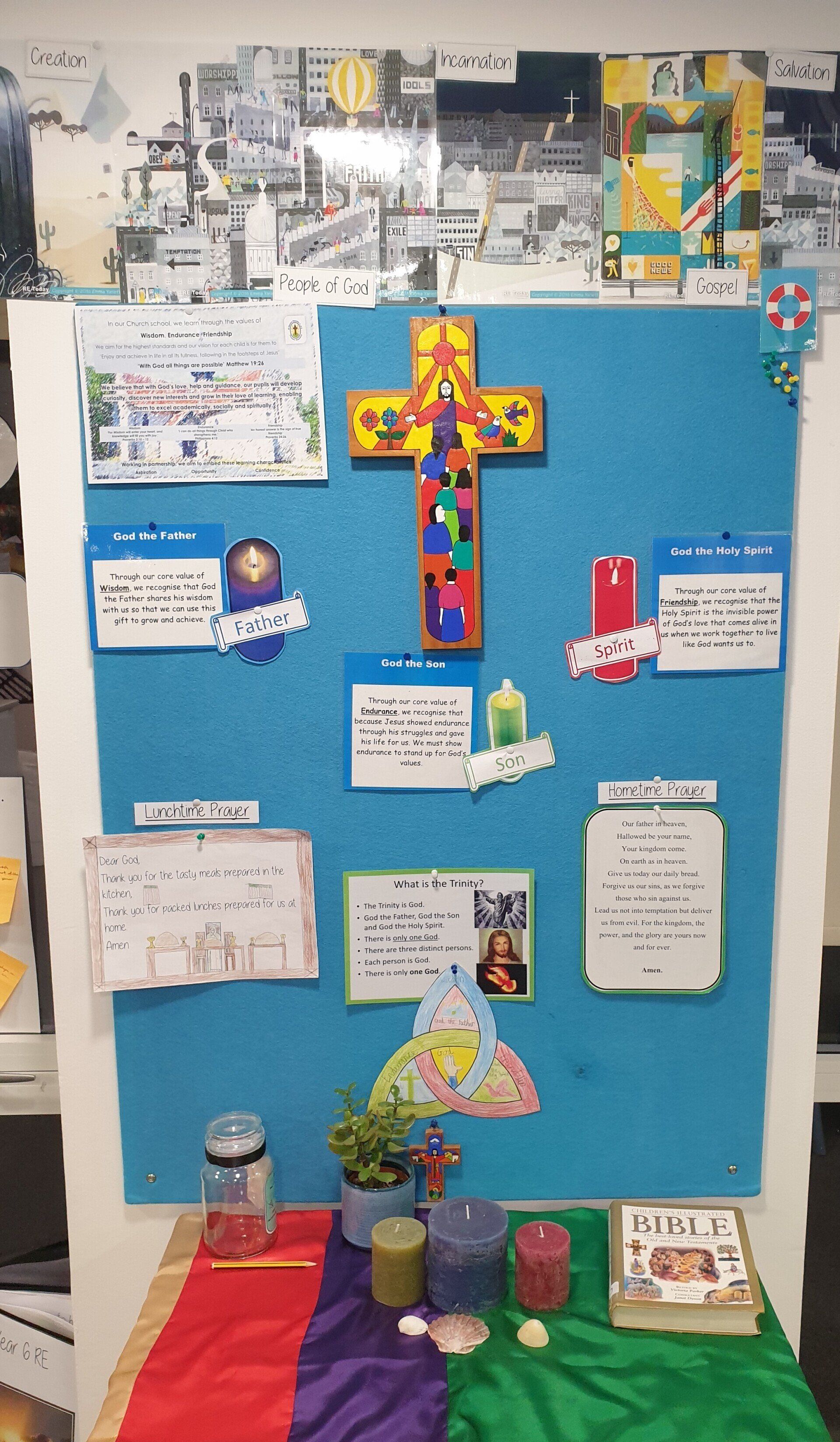 Blue bulletin board with a colorful cross, notes, candles, and a table with a red, purple, and green cloth.