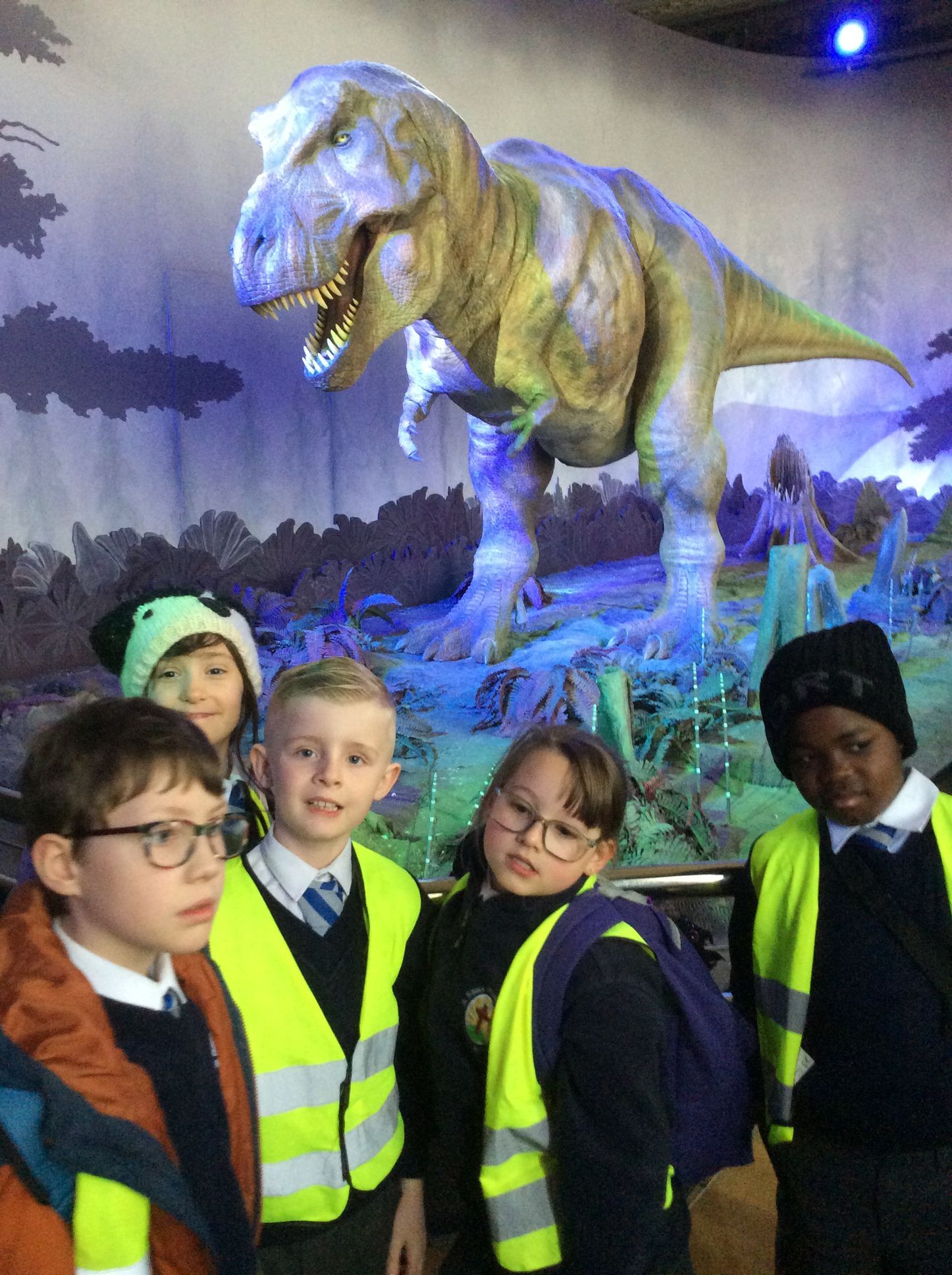 A group of children are standing in front of a dinosaur statue.