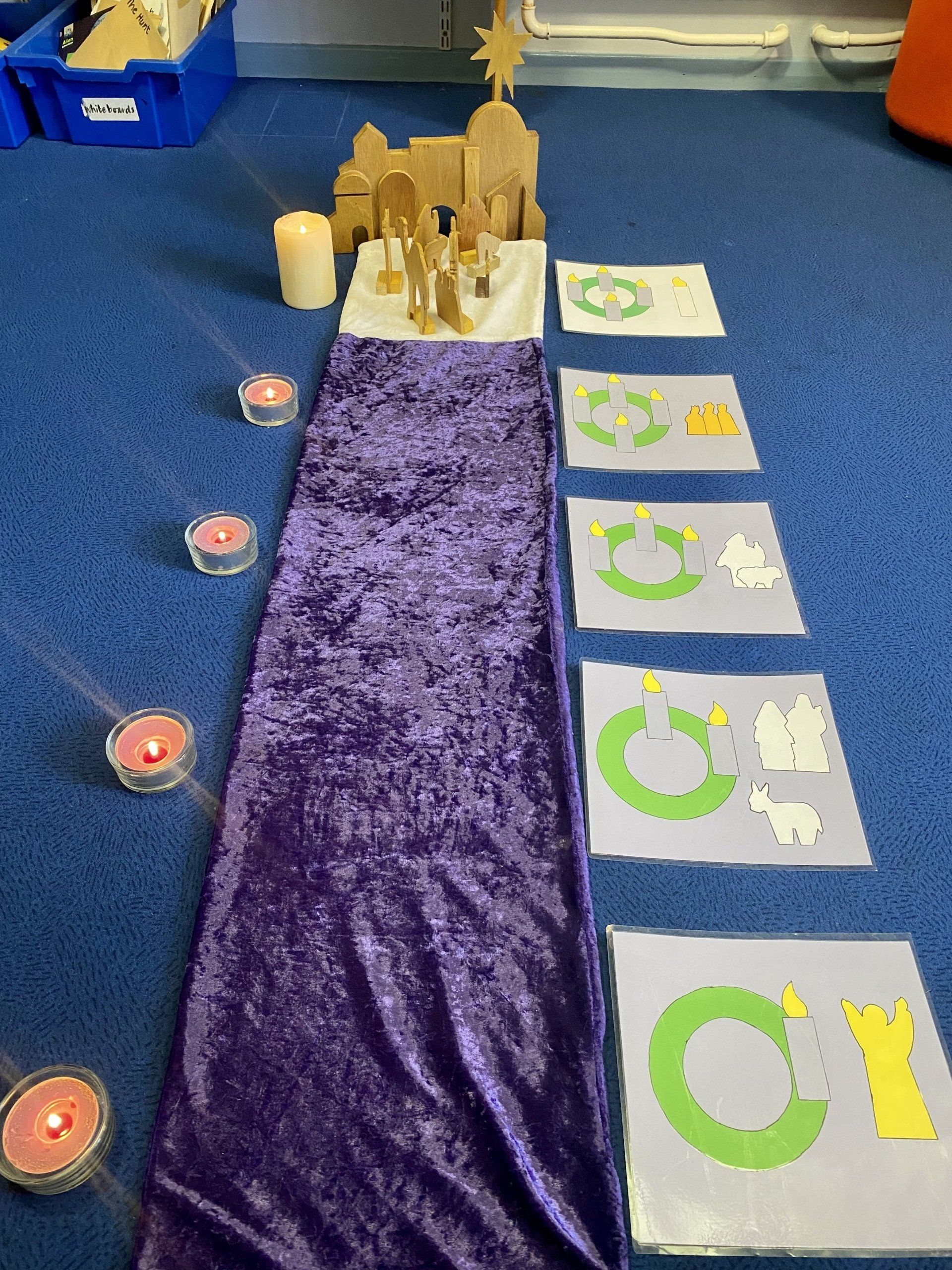 Nativity scene with a purple runner, candles, and artwork on a blue floor.