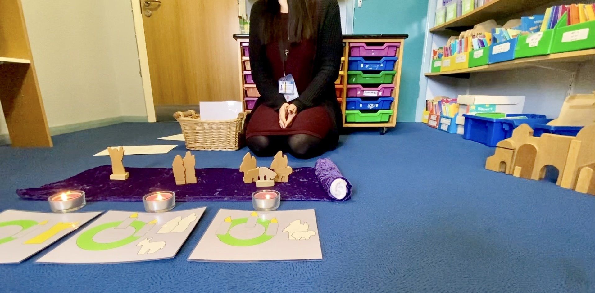 A person kneels in front of lit candles and wooden shapes on a blue carpet.