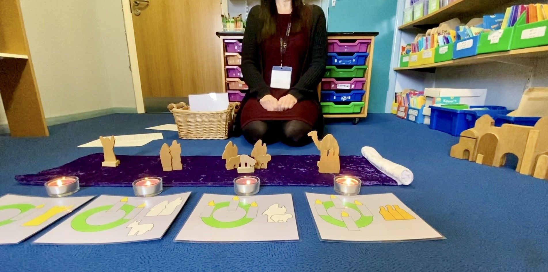 A person sits on a blue carpet in front of lit candles and learning materials.