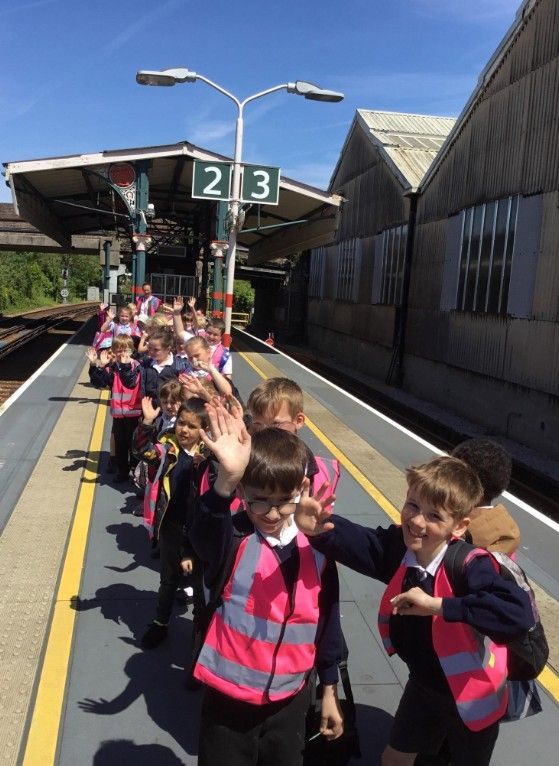 Children in pink safety vests waving on a train platform under sign 213
