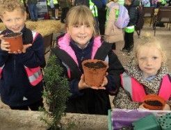 Three children holding small potted plants outdoors at a garden center