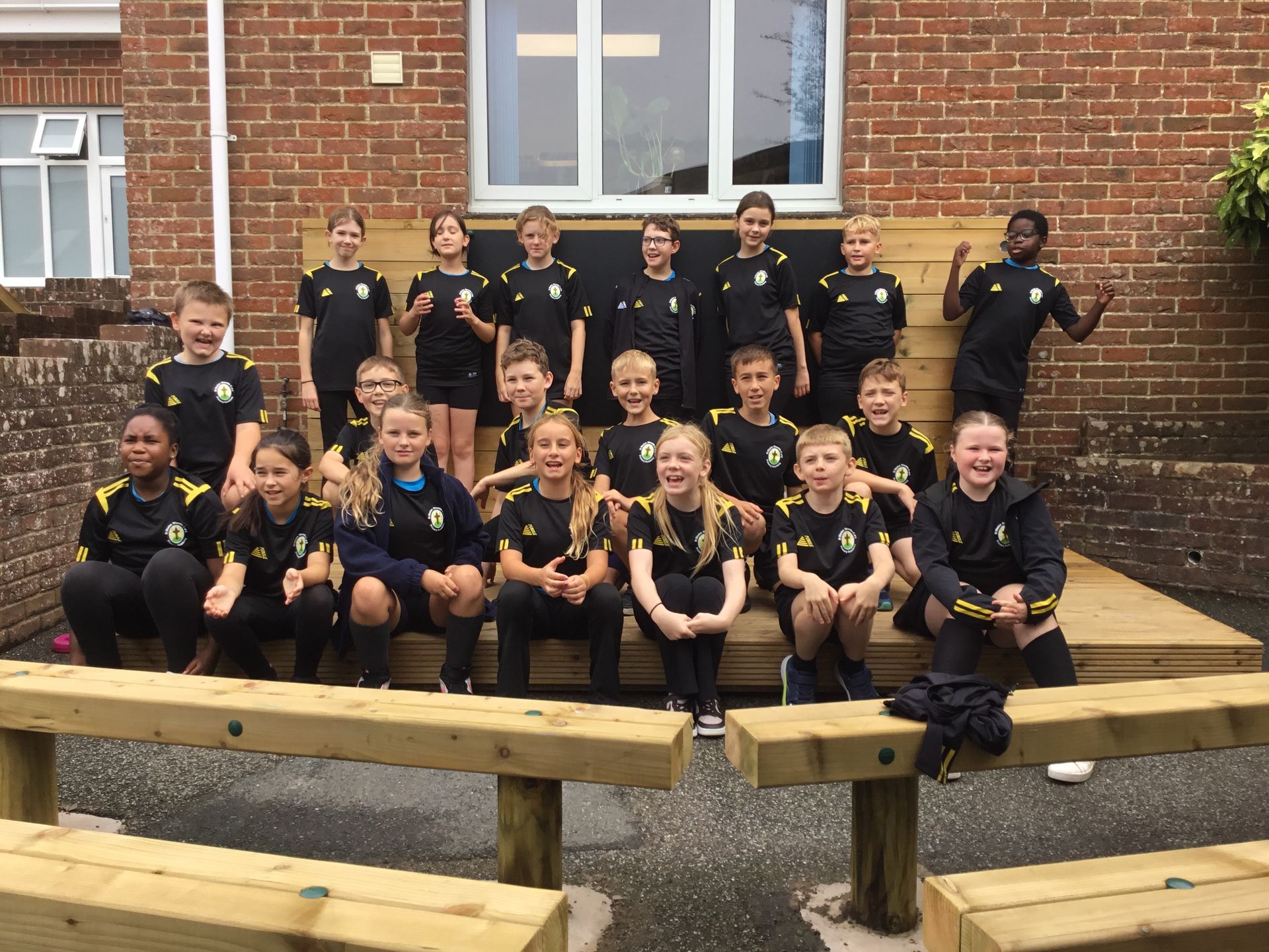 Group of schoolchildren in black uniforms posing on a wooden bench in front of a brick building