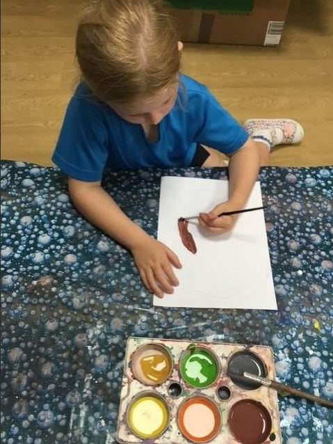 Child painting on white paper with watercolors at a table.