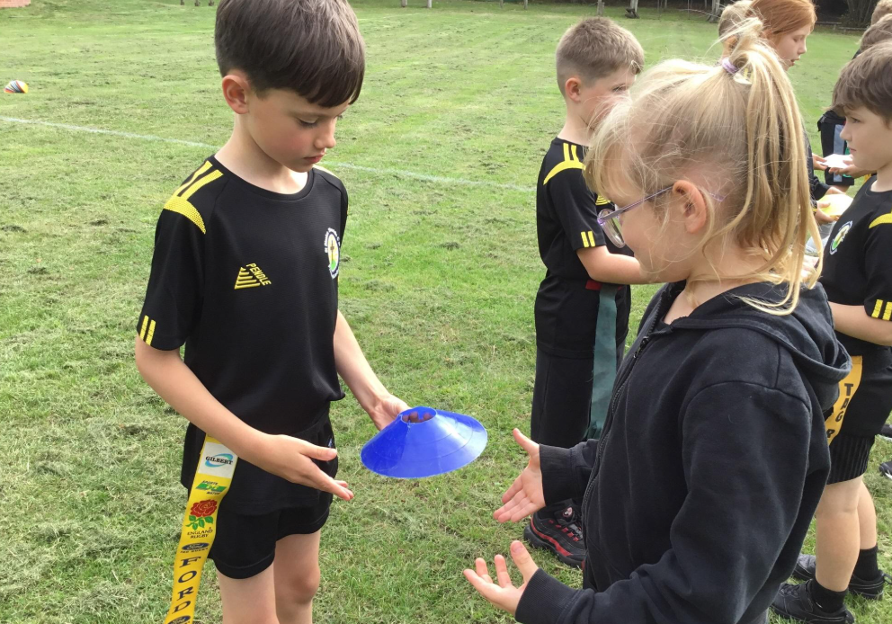 Children in black sports uniforms pass blue cones on a grassy field