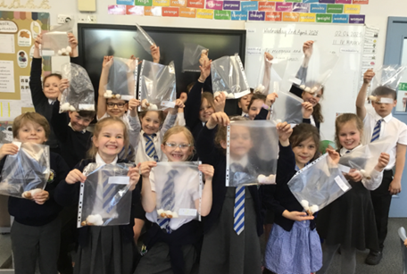 A group of children are holding plastic bags in their hands in a classroom.