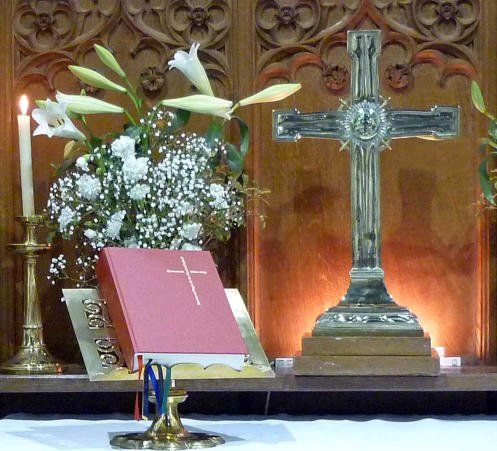 Altar with cross, flowers, lit candle, and Bible. Wooden carved background.