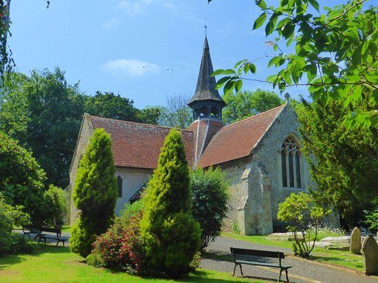 Church with red-tiled roof and tall spire, surrounded by green trees and a grassy lawn, benches visible.