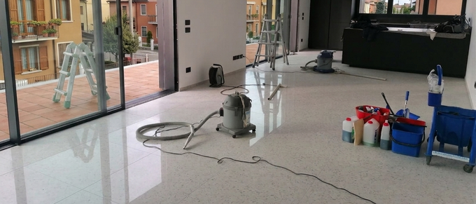 Piccola stanza con una lucidatrice per pavimenti, cavi e prodotti per la pulizia su un pavimento di cemento lucido.