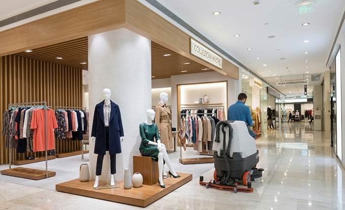 Interno di un negozio di abbigliamento con manichini, appendiabiti e clienti in un luminoso corridoio di un centro commerciale.