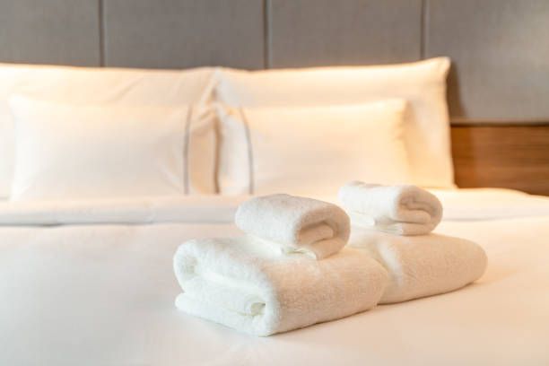 Letto d'albergo ben rifatto con cuscini bianchi, lenzuola e asciugamani arrotolati sopra.