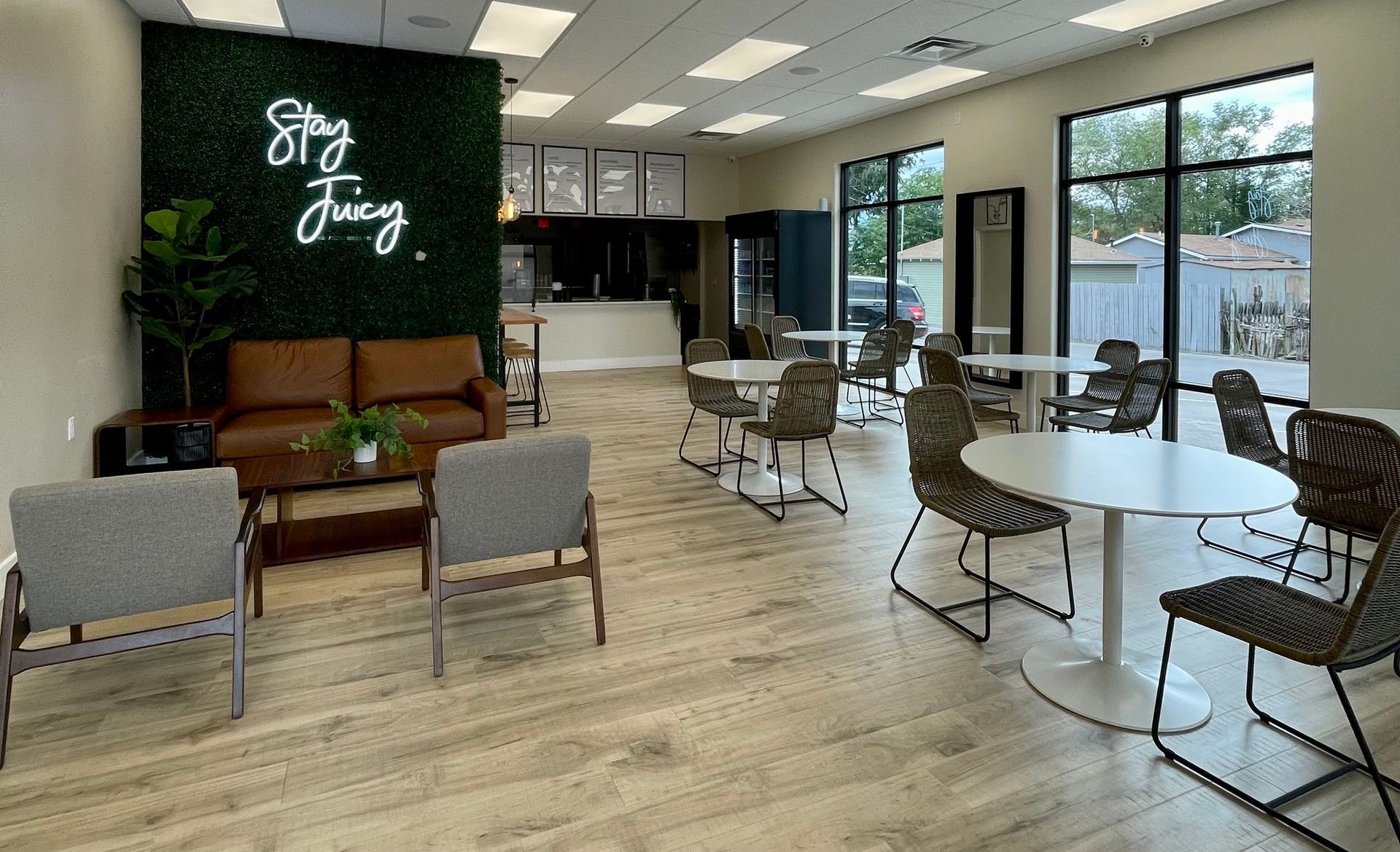 Modern café interior with a brown leather couch, gray chairs, white tables, and a neon