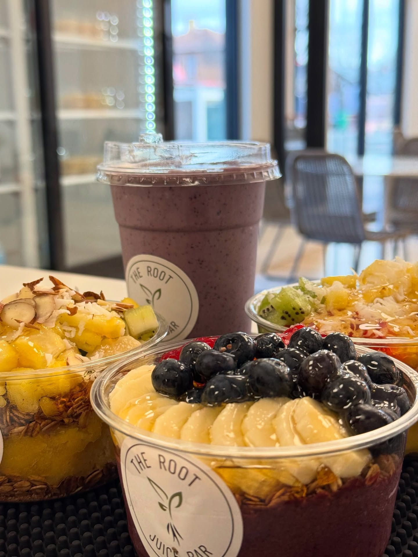 Acai bowls topped with fresh fruit and a purple smoothie in clear plastic containers labeled