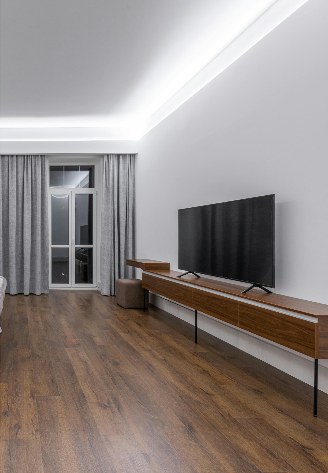 Modern living room with wood floor, gray curtains, and a wall-mounted TV on a long console.