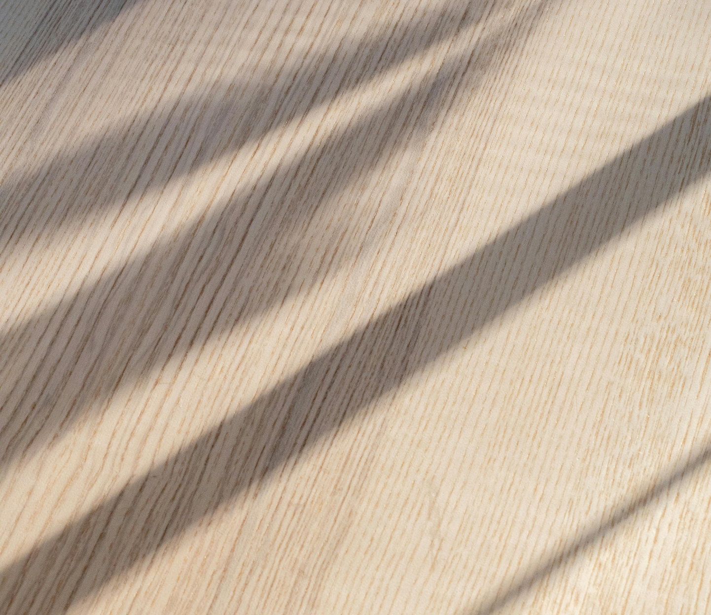 Diagonal shadows across a light wooden surface with fine grain texture