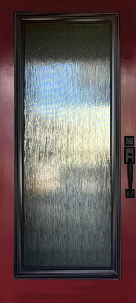 A close up of a glass door with a handle on a red wall.
