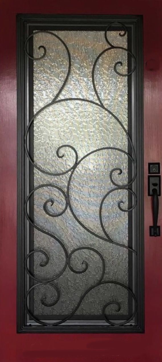 A door with a wrought iron design on it is on a red wall.