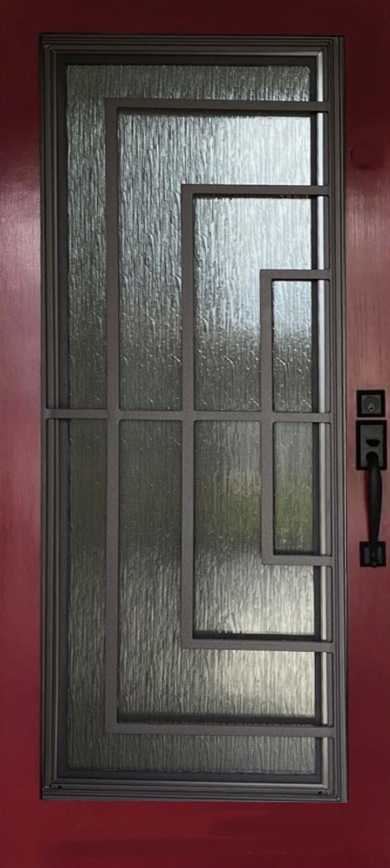 A door with a geometric design on it is on a red wall.