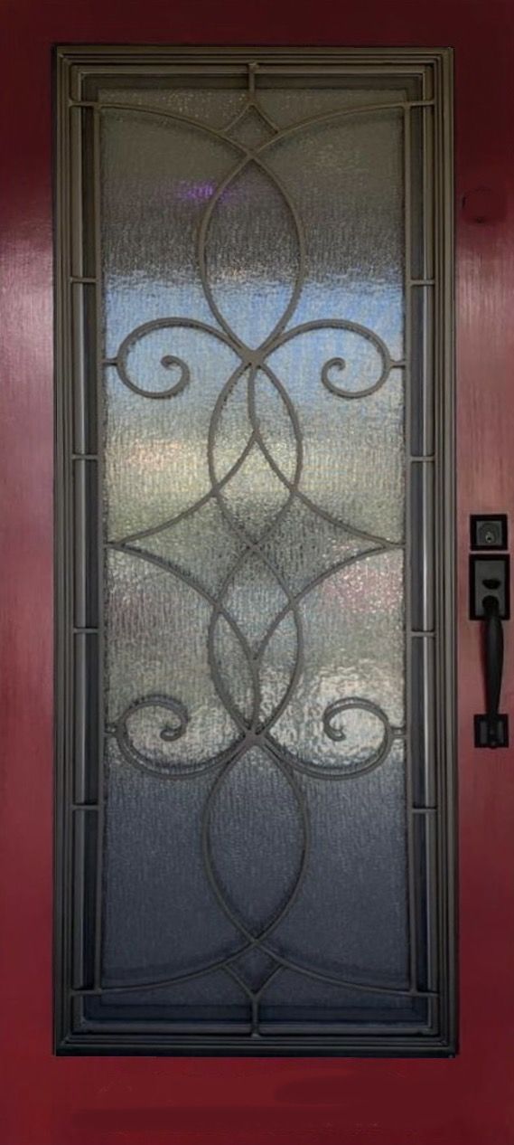 A door with a wrought iron design on it is on a red wall.