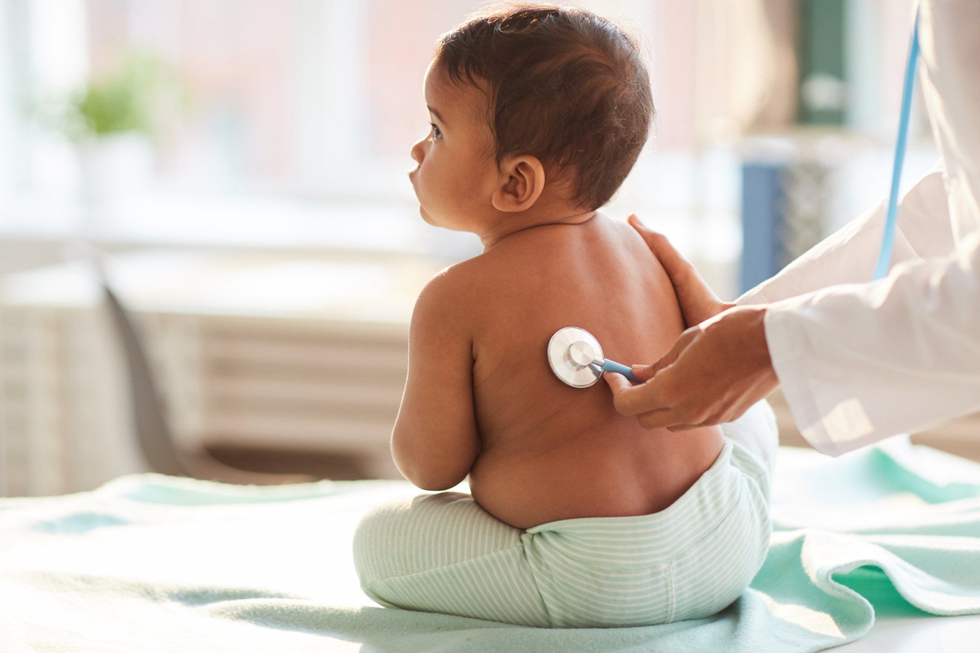 doctor places stethoscope on infant child's back