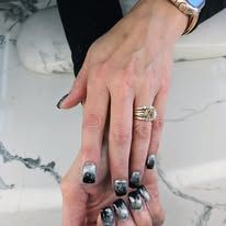 Two manicured hands with black-and-white nails and gold rings over a marble surface