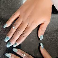 Hands with long glittery blue nails on a dark surface