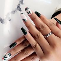 Hands with dark green and white floral nail art on a marble surface