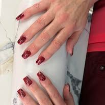 Hands with dark red manicure resting on a white marble surface.