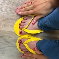Two pairs of feet with red nail polish wearing yellow flip-flops on a wooden floor