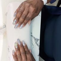 Hands with long silver nails resting on a white marble table.