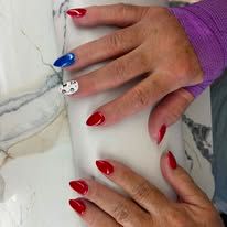Hands with glossy red nails and one blue accent nail, resting on white marble.
