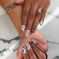 Manicured hands with black, white, and pink patterned nail art and silver rings on a marble surface