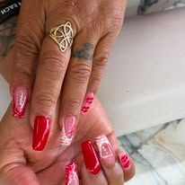Hands with long red and pink manicured nails, wearing a gold ring, resting together on a light surface