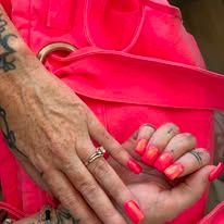 Hand resting on bright pink fabric, showing neon coral nails and rings.