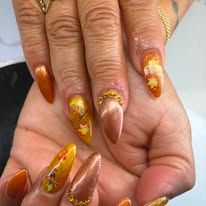 Hand with long brown and gold nail art, featuring marbled yellow designs and glitter accents