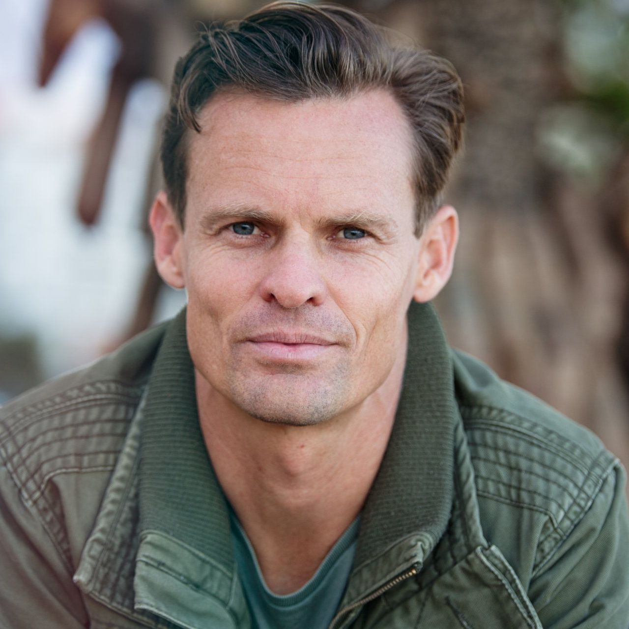 A man in a green jacket is looking at the camera