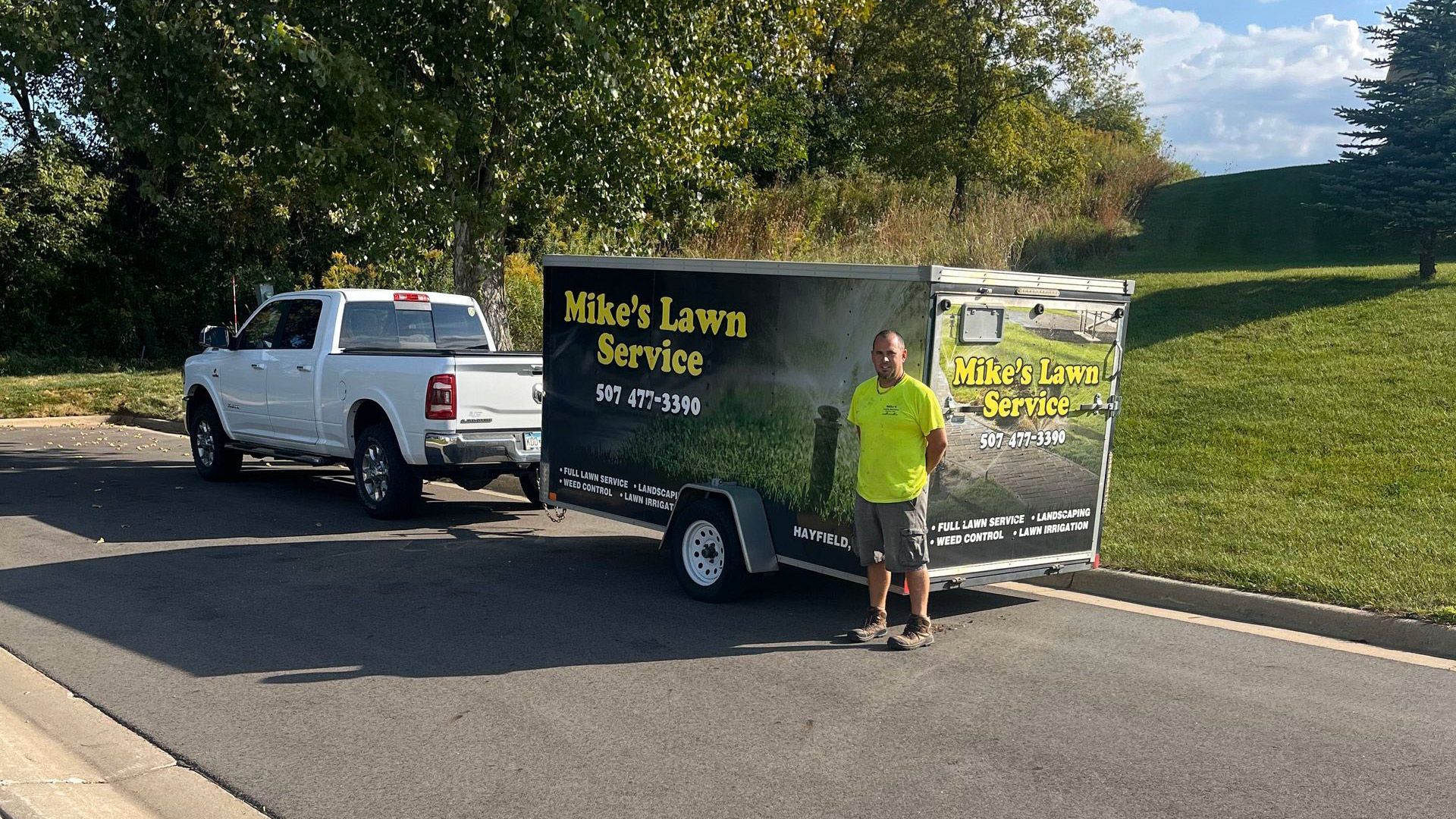 A man is standing next to a trailer that says mike 's lawn service.