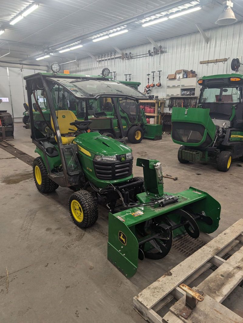 A john deere tractor with a snow blower attached to it is parked in a garage.
